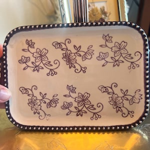 May include: A rectangular ceramic serving tray with a cream-colored base and a dark brown floral pattern. The tray features a dark brown rim decorated with a white dotted pattern and small handles on each side with matching floral designs.