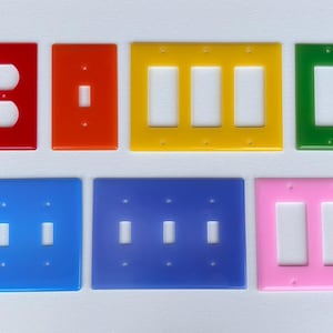 May include: A collection of colorful electrical outlet and switch covers in red, orange, yellow, green, blue, and pink. The covers have various configurations, including single and multiple switch openings.