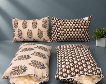 Könnte beinhalten: Vier rechteckige Dekokissen mit Blumenmustern. Zwei Kissen sind beige mit braunen Blumenprints, zwei sind braun mit weißen Blumenprints. Jedes Kissen hat einen sichtbaren Reißverschluss, der eine flauschige, cremefarbene Wollfüllung zeigt.