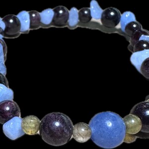 May include: A beaded bracelet featuring a mix of blue, purple, and clear gemstones. The bracelet includes round and irregular-shaped beads in shades of blue, purple, and clear, strung together on a flexible cord. The bracelet is displayed against a black background.