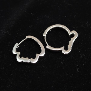 May include: Two silver-colored hoop earrings. One earring has a scalloped edge, while the other has a decorative design. The earrings are displayed against a dark background.