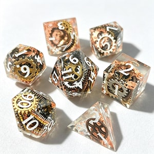 May include: Set of seven polyhedral dice with a steampunk theme. Each die is clear with embedded bronze and silver gears, cogs, and metallic accents. White numbers are visible on each die. The dice are designed for tabletop role-playing games.