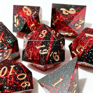 以下が含まれることがあります： 黒いベース、赤い縞模様、金色の数字が特徴の、7つの多面体サイコロのセット。サイコロはグリッター入りの透明樹脂製で、テーブルゲーム用に設計されています。D4、D6、D8、D10、D12、D20、およびパーセンタイルダイスが含まれています。