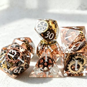 May include: A set of polyhedral dice with a steampunk theme. The dice are clear with copper and gold-colored gears and white numbering. The set includes a d4, d6, d8, d10, d12, and d20.