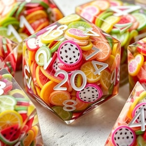 Könnte beinhalten: Ein klarer, vielseitiger Würfel gefüllt mit bunten Fruchtscheiben, darunter Orangen, Zitronen und Drachenfrucht. Weiße Zahlen markieren jede Seite. Die Würfel sind von anderen Würfeln mit ähnlichem Design umgeben.