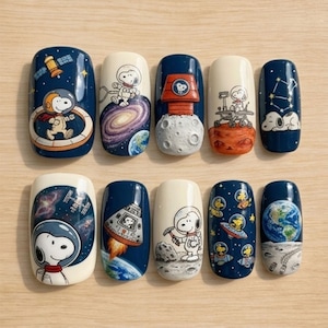 May include: A set of ten artificial nails with space-themed designs. Each nail features Snoopy in various astronaut poses, planets, rockets, and space rovers. The color palette includes navy blue, white, orange, and earth tones, creating a whimsical and detailed aesthetic.