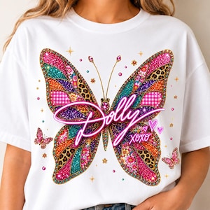 May include: A white t-shirt featuring a large, colorful butterfly graphic with glittery pink, teal, orange, and leopard print patterns. The text "Dolly" is written in a bright pink script across the center, with "XOXO" and small hearts below.