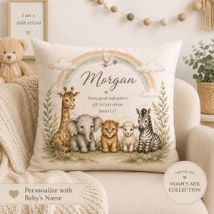 Puede incluir: Un cojín cuadrado con una ilustración impresa de una jirafa, elefante, león, cordero y cebra bajo un arcoíris. El texto dice Morgan, Every good and perfect gift is from above. James 1:17. Una paloma vuela sobre el nombre.