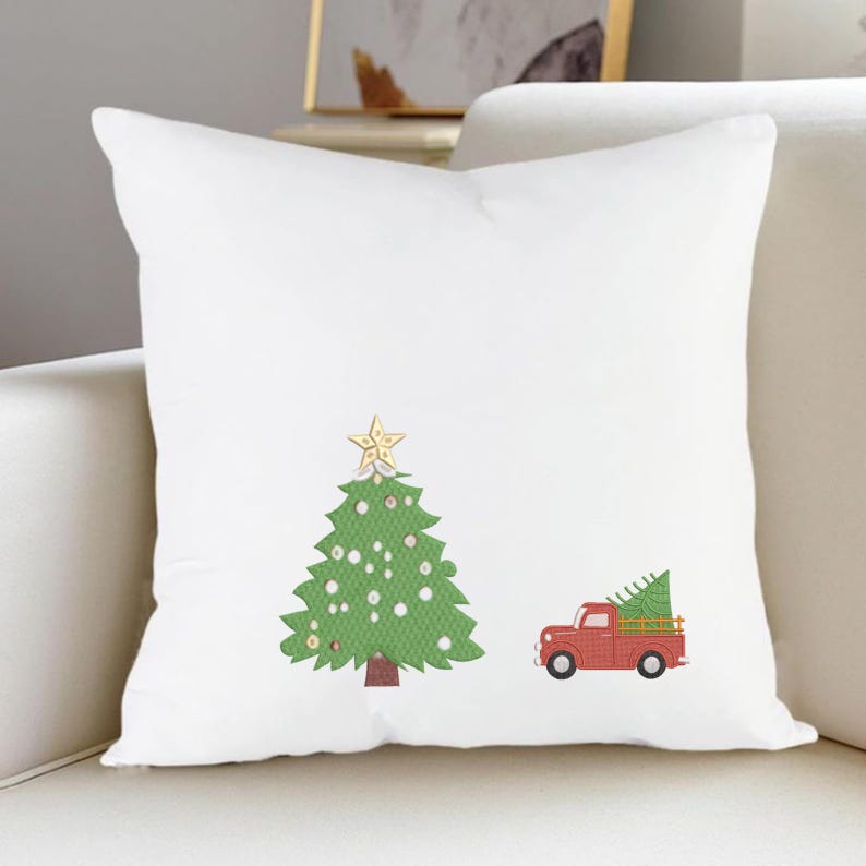K&ouml;nnte beinhalten: Ein wei&szlig;es quadratisches Dekokissen mit einem gr&uuml;nen Weihnachtsbaum, der mit wei&szlig;en Ornamenten und einem goldenen Stern an der Spitze verziert ist, neben einem roten Pickup, der einen kleinen gr&uuml;nen Tannenbaum auf der Ladefl&auml;che tr&auml;gt.