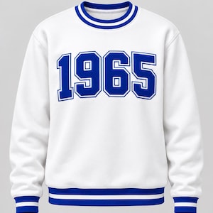 May include: A white long-sleeve sweatshirt featuring the blue text 1965 printed across the chest. The garment has a ribbed crew neckline, cuffs, and hem, each accented with two horizontal blue stripes that contrast against the white fabric base.