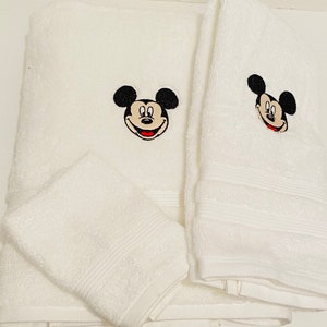 May include: Set of three white bath towels with embroidered Mickey Mouse faces. The towels are soft and absorbent.