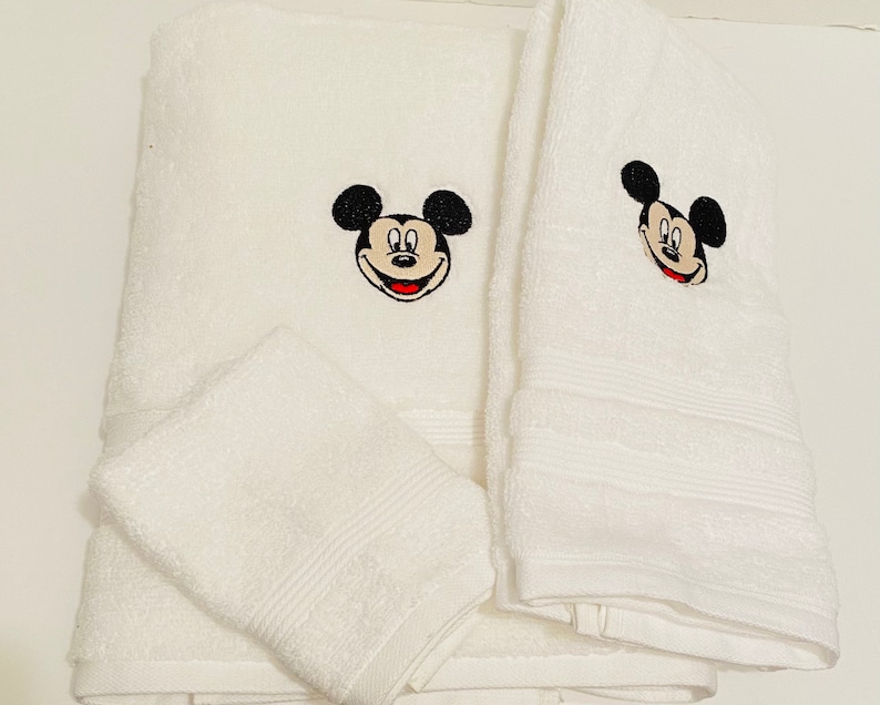 May include: Set of three white bath towels with embroidered Mickey Mouse faces. The towels are soft and absorbent.