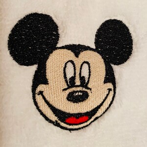 May include: Embroidered image of Mickey Mouse with black ears, a beige face, and a red smile.