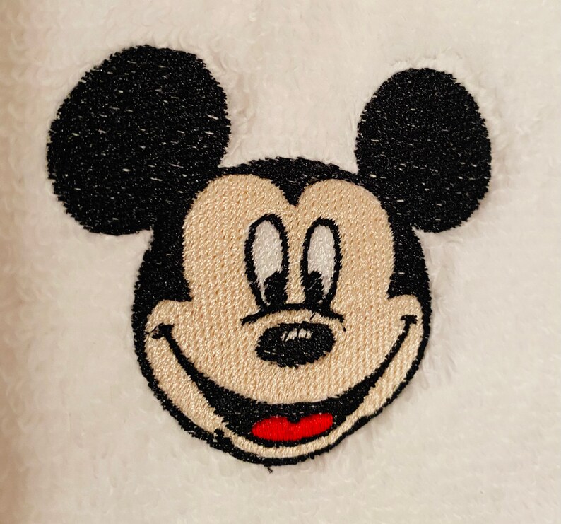 May include: Embroidered image of Mickey Mouse with black ears, a beige face, and a red smile.