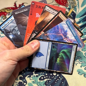 Puede incluir: Una colección de cartas coleccionables de Magic: The Gathering sostenidas en forma de abanico. Las cartas visibles incluyen Mindbreak Trap, Mirkwood Bats, una carta legendaria de J.R.R. Tolkien, Cabal Coffers, Mountain, Fierce Guardianship y una carta de Isla.