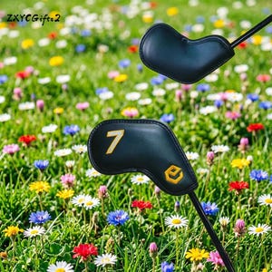 Puede incluir: Dos fundas negras para la cabeza de un palo de golf con n&uacute;meros y logotipos amarillos se muestran sobre un fondo de un prado vibrante lleno de coloridas flores silvestres. Las fundas est&aacute;n sobre ejes negros.