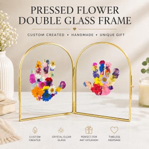 May include: A double glass frame with a gold metal arch design. The frame contains two hand-shaped arrangements of pressed flowers in various colors. Text on the frame reads "PRESSED FLOWER DOUBLE GLASS FRAME".