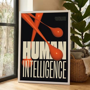 May include: A framed poster with the words "HUMAN INTELLIGENCE" in large, off-white block letters. The background is black, with orange, abstract shapes. The poster is in a white frame and is displayed near a window.