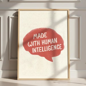 May include: A framed wall art print featuring a textured off-white background and a central red, brain-shaped speech bubble. The text "MADE WITH HUMAN INTELLIGENCE" is printed in white, bold, sans-serif capital letters inside the red shape.