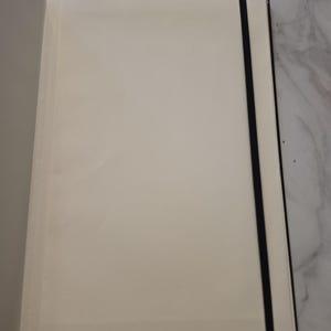 May include: An open notebook with blank, off-white pages and a black elastic band closure. The notebook features a sturdy black cover and is positioned to show the interior paper surface, which is smooth and unlined, providing a clean writing area.