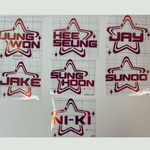 May include: Seven individual vinyl decals on clear transfer tape, each featuring a red-to-orange gradient star outline and the names Jung Won, Hee Seung, Jay, Jake, Sung Hoon, Sunoo, and Ni-Ki in a bold, blocky, sans-serif font style.