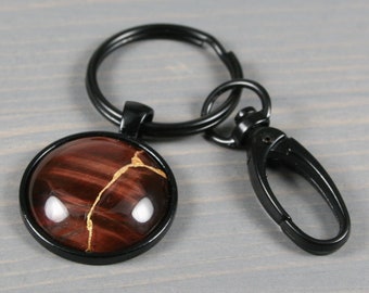 Kintsugi repaired red tiger eye key chain in a black bezel setting with swivel lobster claw