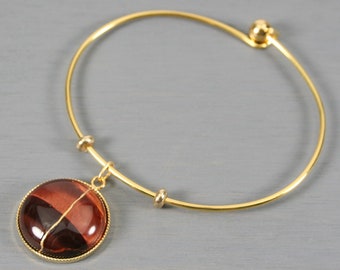 Kintsugi repaired red tiger eye charm on a gold plated bangle bracelet