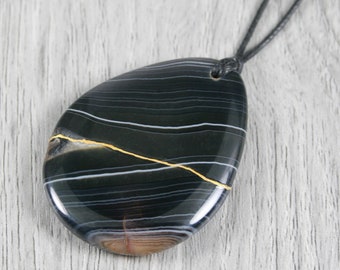 Kintsugi repaired black banded agate teardrop pendant on an adjustable black cotton cord necklace