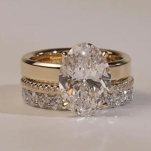 Peut inclure: Une pile de trois bagues en or avec une grande pierre centrale taille ovale aux facettes brillantes. L'ensemble comprend un anneau en or lisse, une fine bague pavée de diamants et un anneau plus large serti de diamants taille brillant.