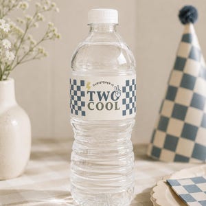 May include: A clear plastic water bottle with a white cap and a custom label. The label features a blue and white checkered pattern, a yellow lightning bolt, a peace sign, and the text "CHRISTOPER IS TWO COOL" in blue and green lettering.