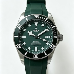 May include: A Tudor Pelagos watch featuring a dark green dial and matching green rubber strap. The watch has a black unidirectional rotating bezel with white numerals, a date window at the three o'clock position, and luminous hour markers.