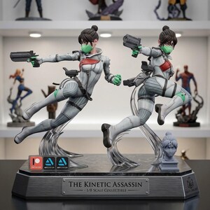 May include: Two statues of a female character in a dynamic pose, holding a gun. The figures wear a white and gray suit with red accents and a green face mask. The base reads "The Kinetic Assassin - 1/8 Scale Collectible."