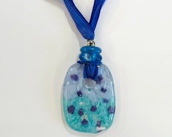 May include: A blue and white glass pendant with a silver and blue bead accent. The pendant is attached to a blue ribbon.