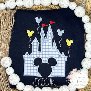 May include: A navy blue sweatshirt with an embroidered design of a blue and white checkered castle with Mickey Mouse ears in the front. The castle has yellow and blue balloons with red flags. The name "JACK" is embroidered below the castle.