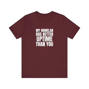 May include: A maroon short-sleeved t-shirt featuring the white text MY HOMELAB HAS BETTER UPTIME THAN YOU printed in a bold, sans-serif font on the centre of the chest. The garment has a crew neckline and a standard, straight-cut silhouette.