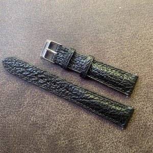 K&ouml;nnte beinhalten: Schwarzes Uhrenarmband mit strukturierter Oberfl&auml;che und silberfarbener Schnalle. Das Armband besteht aus strapazierf&auml;higem Material und hat N&auml;hte an den Kanten. Das Uhrenarmband ist f&uuml;r eine Standarduhr konzipiert.
