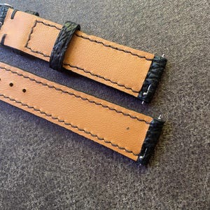 K&ouml;nnte beinhalten: Nahaufnahme von zwei Uhrenarmb&auml;ndern. Die Armb&auml;nder bestehen aus hellbraunem Leder mit schwarzen Kanten und N&auml;hten. Die schwarzen Kanten haben ein strukturiertes Aussehen. Die Armb&auml;nder liegen auf einer grauen Oberfl&auml;che.