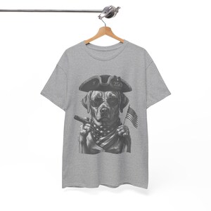 May include: A heather gray short-sleeve t-shirt featuring a black and white graphic of a dog wearing a tricorn hat and sunglasses, holding a cigar, and wearing a star-patterned bandana, with a small American flag visible in the background.