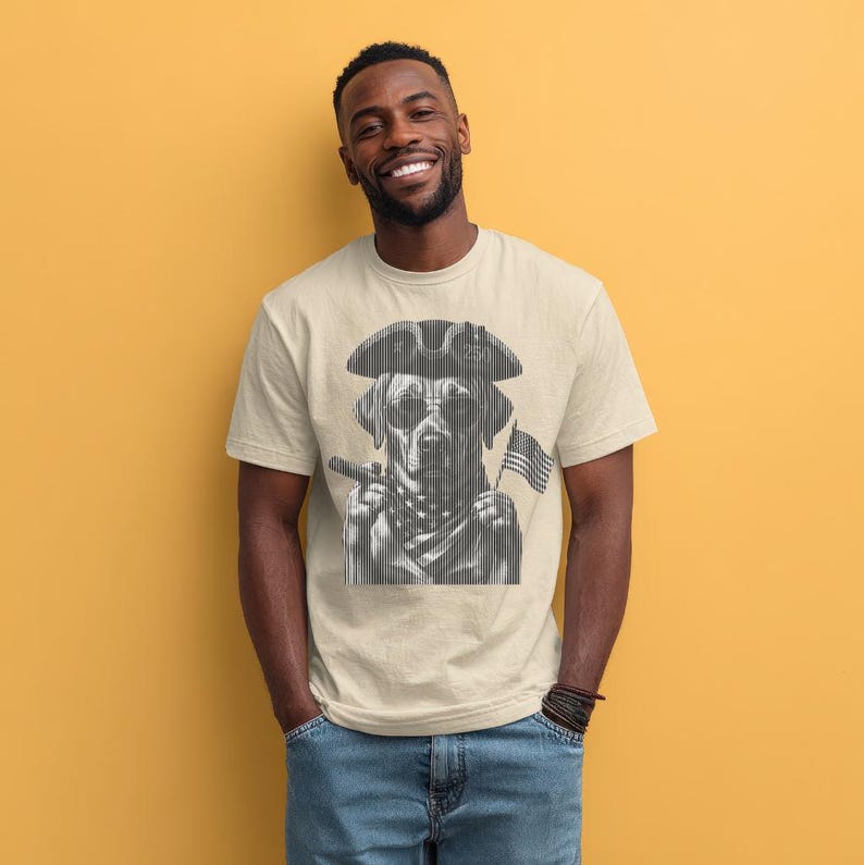 May include: A beige short-sleeved t-shirt featuring a black and white graphic print of a dog wearing a tricorn hat and sunglasses. The dog is holding a small American flag and a cigar, rendered in a vertical line art style on the chest.