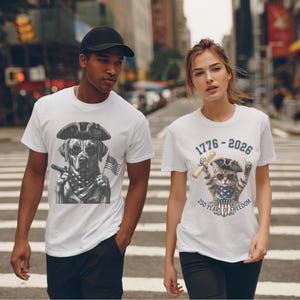 May include: Two white t-shirts featuring patriotic graphics. The left shirt displays a black and white dog in a tricorn hat with sunglasses and an American flag. The right shirt shows a cat in a tricorn hat with sunglasses, a scroll, and the text 1776-2026 250 YEARS OF FREEDOM.