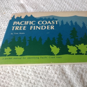 May include: A rectangular pocket manual titled Pacific Coast Tree Finder by Tom Watts. The cover features a graphic illustration of a forest in shades of blue and green against a light background, with the text a pocket manual for identifying Pacific Coast trees.