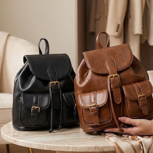 Puede incluir: Dos mochilas, una negra y otra marrón, cada una con una solapa superior con cierre de hebilla, un compartimento principal con cordón y dos bolsillos delanteros con correas de hebilla. Las bolsas tienen un acabado liso y un asa superior.