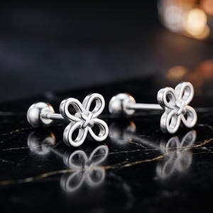 May include: A pair of silver-toned stud earrings featuring a four-petaled openwork flower design with a small cross detail at the center. Each earring has a straight post and a round ball backing, showcasing a polished metallic finish throughout.