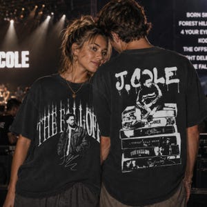 May include: A black short-sleeve t-shirt featuring a white graphic of J. Cole on the front with the text THE FALL OFF. The back displays a white graphic of J. Cole sitting on a stack of albums with the text J. COLE and various album titles.