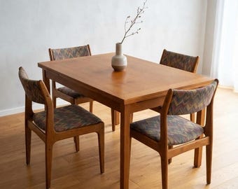 May include: A rectangular wooden dining table with four matching chairs. Each chair features a seat and backrest upholstered in a multi-colored chevron patterned fabric. A small, two-toned ceramic vase sits in the center of the table.
