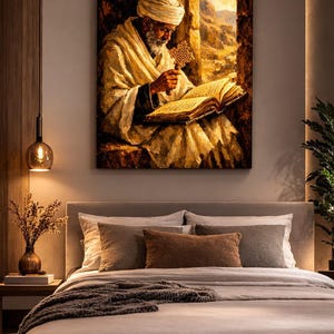 Puede incluir: Una impresi&oacute;n en lienzo enmarcada representa a una persona mayor leyendo un libro junto a una ventana. La persona lleva un turbante y una t&uacute;nica blancos, sosteniendo un objeto en forma de cruz. La obra de arte est&aacute; en tonos c&aacute;lidos, con una cama en primer plano.