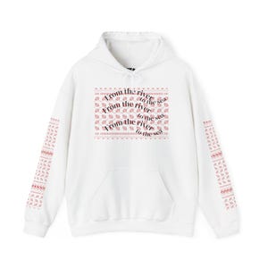 May include: White hoodie with a front pocket and drawstring. The front features the text "From the river to the sea" in a repeating pattern. The sleeves have a repeating pattern in red.