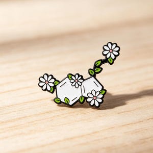 May include: A metal enamel pin shaped like a chemical molecular structure with white hexagonal and pentagonal centers, accented by small white daisy flowers with pink centers and green leaves, outlined in black metal throughout the design.