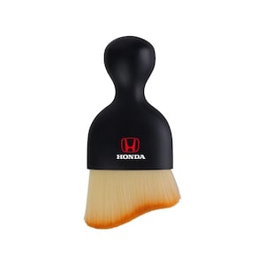 May include: A black brush with a rounded handle and a fan-shaped brush head. The brush head has light beige bristles with an orange gradient at the tips. The Honda logo is printed in red and white on the brush.