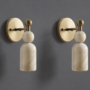 May include: A pair of wall sconces featuring a circular brushed brass backplate, a horizontal arm, and a vertical post topped with a small brass sphere. Below the sphere is a spherical marble accent and a cylindrical marble light shade.